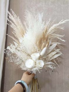 a person is holding a bouquet with white flowers and feathers on the stems in front of a curtain