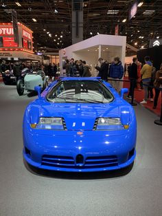 a blue sports car is on display in a showroom with people looking at it