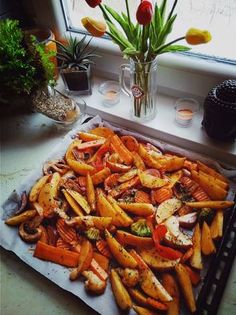 a tray full of cooked carrots on a counter next to a vase with tulips in it