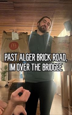 a man holding up a bag with the words past alger brick road, i'm over the bridge