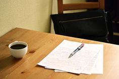 a cup of coffee sitting on top of a wooden table next to a pen and paper