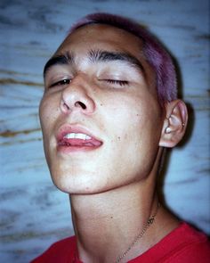 a young man with pink hair and piercings on his ears is looking up to the sky