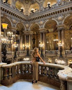 a woman standing on top of a balcony next to chandeliers and lights in a building