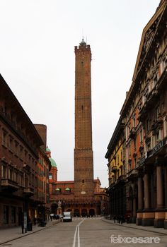 a tall clock tower towering over a city next to tall brick buildings on either side of a street