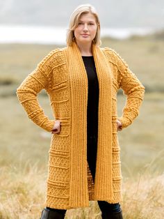 a woman standing in tall grass with her hands on her hips wearing a yellow cardigan