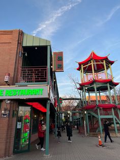 people are walking around in front of some buildings with red and green awnings