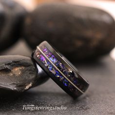 two wedding bands with purple and blue flowers inlays are sitting next to some rocks