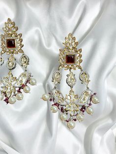 Introducing our exquisite Gold Indian Earrings adorned with radiant rubies and mesmerizing uncut polki, a true testament to timeless elegance and traditional craftsmanship. These captivating earrings are designed to enhance your beauty and add a touch of regal charm to any ensemble. 🌟 Features: 🔸 Material: High-quality gold-plated metal 🔸 Gemstones: Rich red rubies and sparkling uncut polki 🔸 Length: Gracefully long, these earrings dangle elegantly 🔸 Colors: Available in three enchanting sh Red Chandbali Jhumkas With Intricate Design, Red Kundan Jhumkas With Intricate Design, Bollywood Ruby Jhumkas For Festivals, Ruby Bollywood Jhumkas For Festivals, Gold Ruby Chandbali Bridal Earrings, Gold Chandbali Bridal Earrings With Ruby, Ruby Chandbalis For Celebration In Temple Jewelry Style, Ruby Temple Jewelry Chandbalis For Celebration, Bollywood Ruby Jhumkas With Latkans