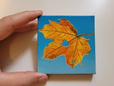 a painting of a leaf is being held by someone's hand on a table