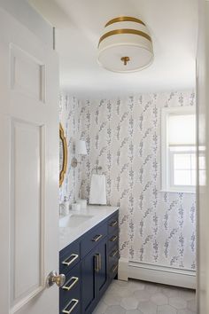 a bathroom with blue cabinets and wallpaper on the walls is pictured in this image