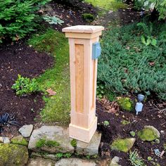 a wooden post sitting in the middle of a garden next to some rocks and plants