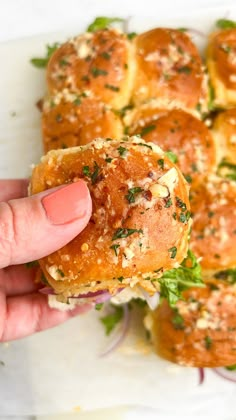 a person is holding up a sandwich with meat and herbs on it, in front of other rolls