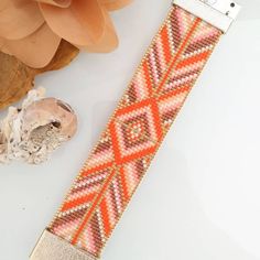 an orange and pink beaded watch strap next to a flower on a white surface