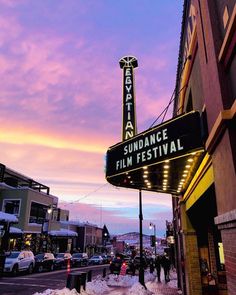 a theater sign is lit up on the side of a building with cars parked in front