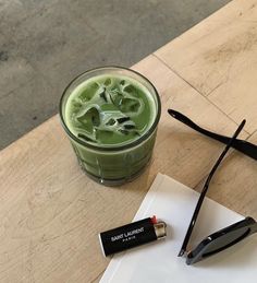 a green drink sitting on top of a wooden table next to a pair of scissors