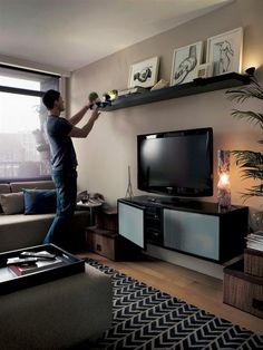 a man standing in front of a tv on top of a wooden shelf next to a window