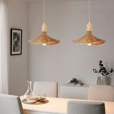 two pendant lights hanging over a dining table in a room with white walls and chairs