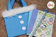 a blue bag with buttons and a pen on it next to a notepad that has a penguin sticker on it