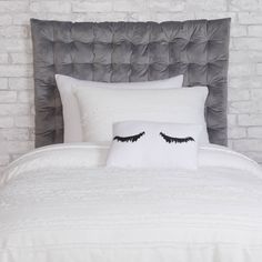 a white bed with two pillows on top of it next to a gray headboard