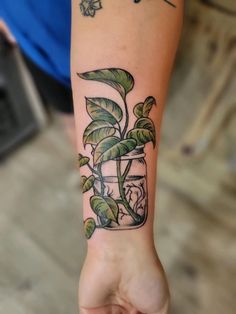 a person's arm with a plant in a jar tattoo on the left wrist