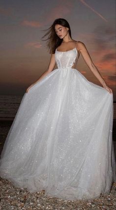 a woman in a white wedding dress standing on the beach at sunset with her hair blowing in the wind