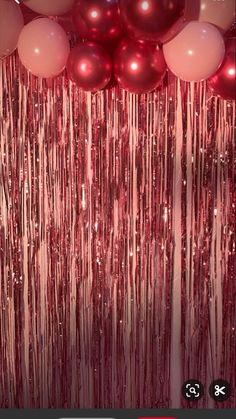 balloons and streamers hanging from the ceiling in front of a red curtain with pink balls