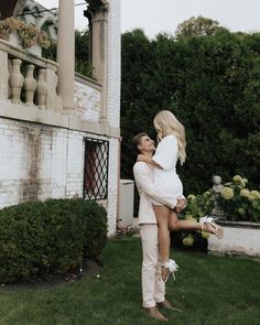 a man holding a woman on his back in front of a white brick building and green grass