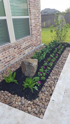 a rock in the middle of a garden bed next to a brick wall and window