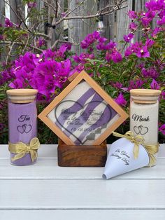 some purple flowers and two jars on a white table next to each other with writing on them