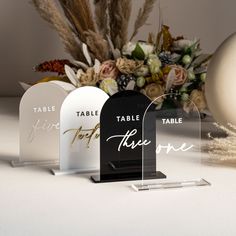 three clear acrylic signs sitting on top of a table next to a vase filled with flowers