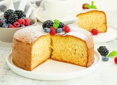 a white plate topped with a slice of cake and berries next to another piece of cake