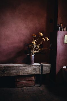 a wooden bench sitting in front of a purple wall with dried flowers on top of it