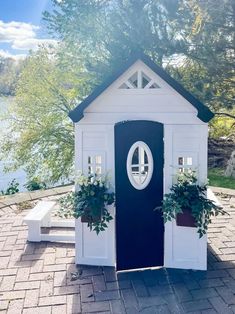 a black and white outhouse with potted plants on the front door is shown