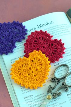 three crocheted hearts sitting on top of an open book next to pair of scissors