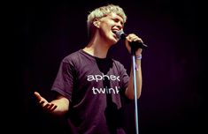 a young man singing into a microphone while wearing a t - shirt that says apprex twin