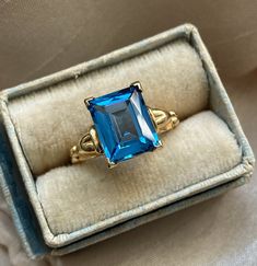 Beautiful rich blue gemstone vintage ring. The color of the blue is absolutely dazzling! The ring dates to the 1940s - 1960s approximately.  Solid 10K yellow gold. Emerald cut gemstone tests as topaz on my at-home SmartPro Gem Tester but looks more like it could be blue spinel, especially judging by the older setting and the high hardness rating. I am not a Gemologist.  Signed and tested real 10K gold. Size 5 US; resizable by your local jeweler.  Measures 10 mm tall, see all photos. Main photo is enlarged/zoomed-in to show you details. In great used, vintage pre-owned condition. Slight rattle when shaken but the stone is secure and in lovely condition for its age. Light normal patina/wear to mount.  See you on Instagram @luxcharmjewelry xo Blue Emerald Classic Promise Ring, Vintage Blue Sapphire Promise Ring, Vintage Emerald Cut Birthstone Rings, Vintage 14k Gold Birthstone Ring With Center Stone, Vintage Emerald Ring For Promise, Vintage 14k Gold Sapphire Birthstone Ring, Antique 14k Gold Topaz Ring, Vintage Sapphire Rings Stamped 14k, Vintage Blue Oval Sapphire Ring