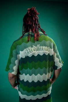 a man with dreadlocks standing in front of a green wall wearing a striped shirt