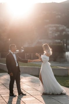 a bride and groom dancing on the sidewalk in front of some buildings at sunset or sunrise