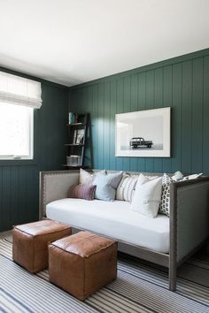 a living room with green walls and white couches, striped rugs and two stools