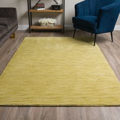 a living room area with a blue chair and yellow rug on the hardwood flooring