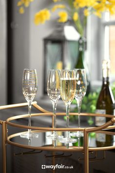 four wine glasses sitting on top of a gold tray with yellow flowers in the background