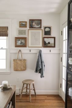 a wooden stool sitting under a window next to a wall with pictures on the wall