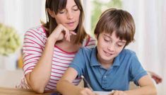 a woman helping a boy with his homework at the table in front of him,