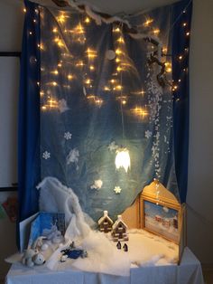 a christmas display with lights and stuffed animals on the table in front of a blue curtain