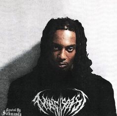 a man with dreadlocks standing in front of a wall wearing a black hoodie