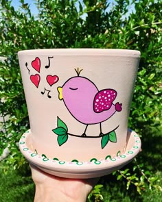 a hand holding up a cup with a bird painted on the side and hearts in the background