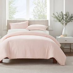 a bed with pink sheets and pillows in a white room next to a window,