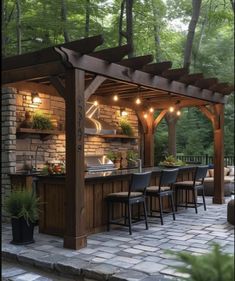 an outdoor kitchen and bar with lights on the roof, surrounded by stone pavers