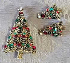 three christmas tree brooches sitting on top of a white cloth