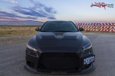 the front end of a black sports car parked in a parking lot near a red and white striped fence